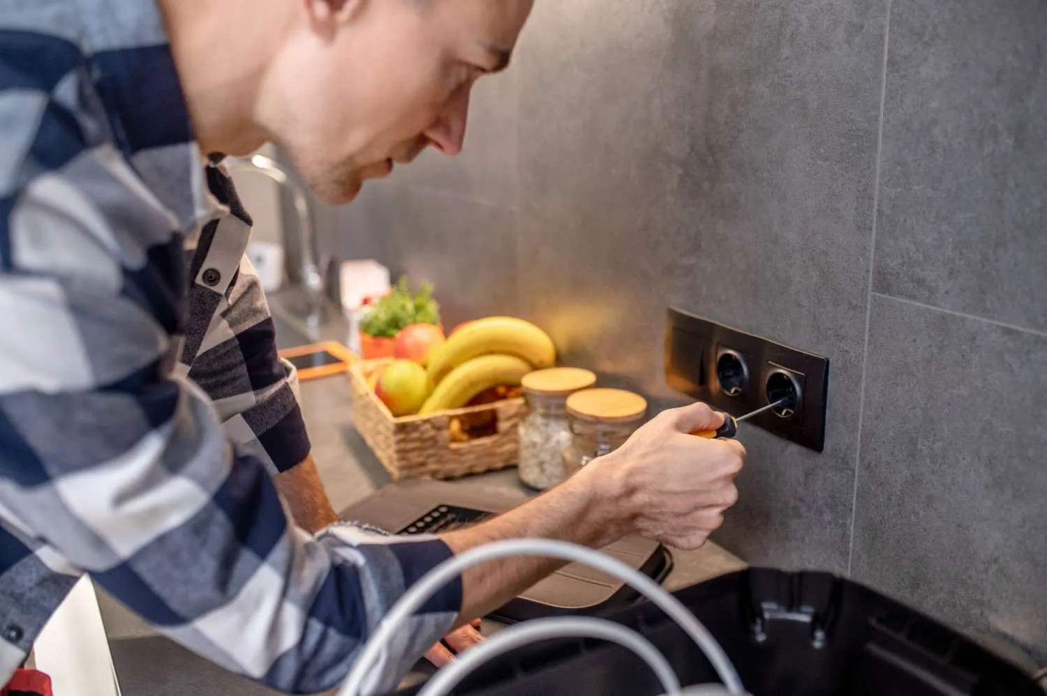 Technician testing a kitchen wall outlet with a screwdriver