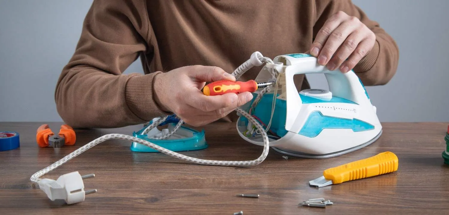 Hands fixing a steam iron with a screwdriver