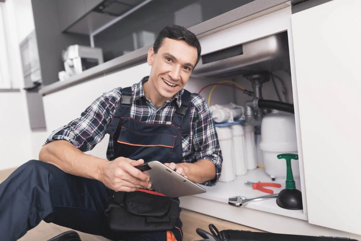 Smiling technician with a clipboard beside a kitchen sink cabinet